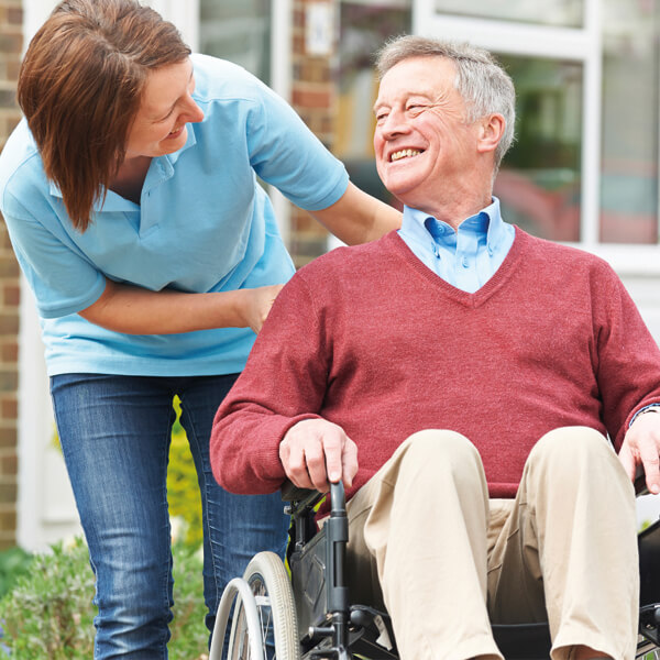 eine Betreuerin und ein im Rollstuhl sitzender Senior beim Spaziergang