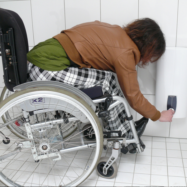 eine im Rollstuhl sitzende Frau reguliert einen Boiler