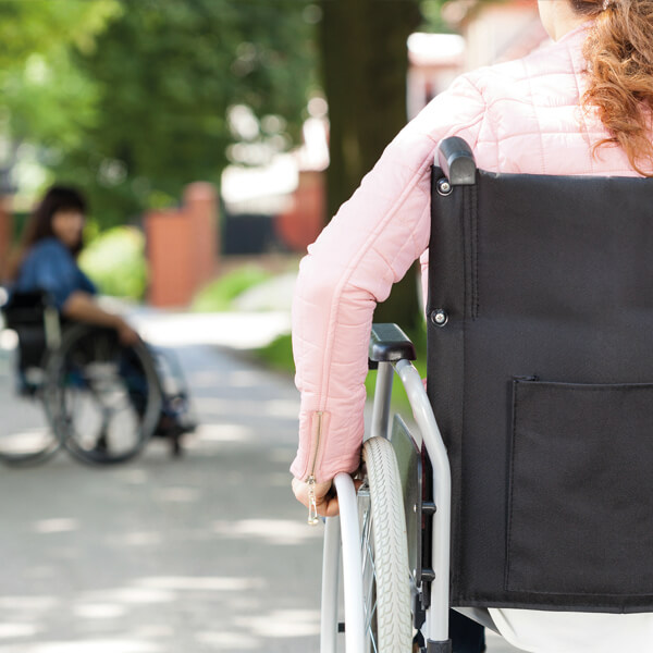 eine Rollstuhlfahrerin bewegt sich auf eine andere, einsam erscheinende Rollstuhlfahrerin zu